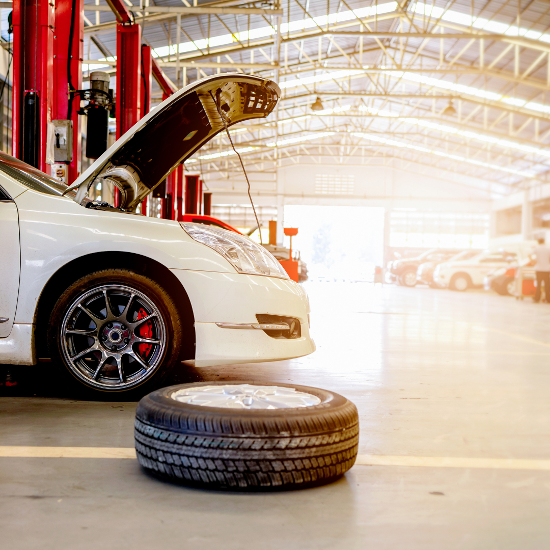 White car in a mechanic’s auto body shop with a tire on the floor.