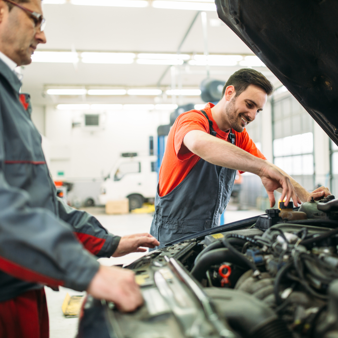 Two auto mechanics inspecting a car’s engine in a garage.